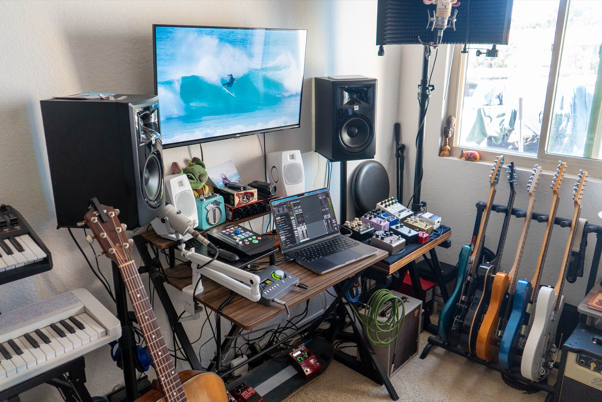 The studio desk: monitors, a laptop, pedals and a row of guitars by the window
