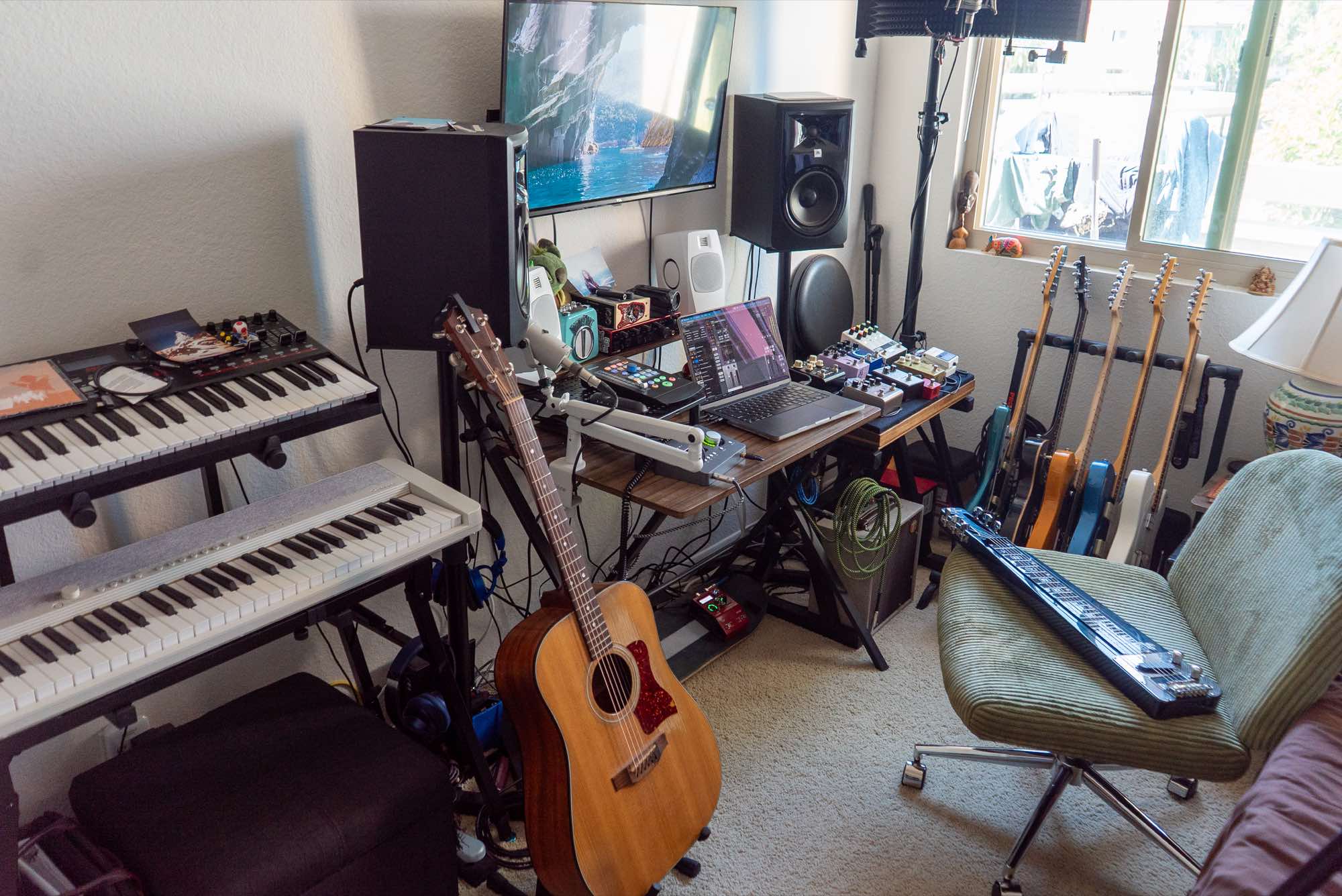 Keyboards, an acoustic guitar and the desk, with the green chair by the guitar rack