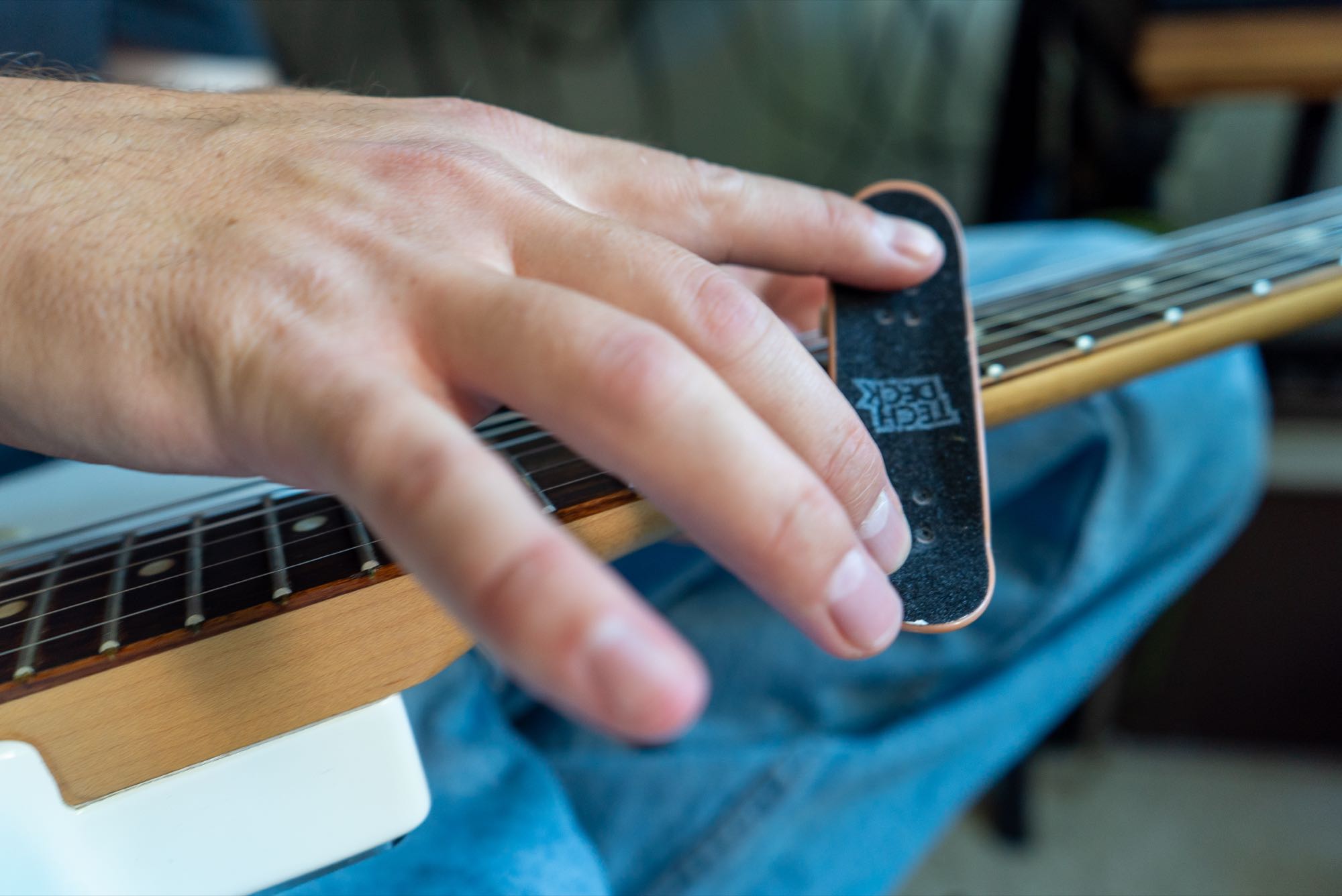 A hand on a guitar neck holding a tiny fingerboard skateboard